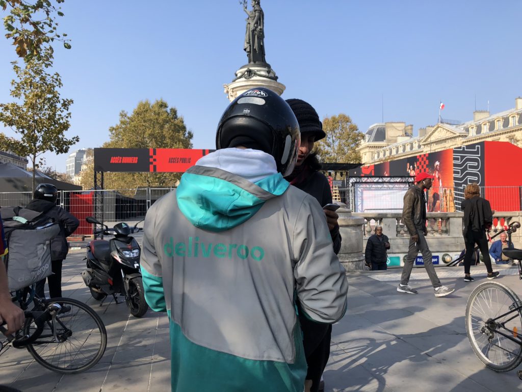 En tenue de travail, une trentaine de livreurs se sont réunis, place de la République à Paris, pour revendiquer une hausse de leurs revenus. // Source : Numerama En tenue de travail, une trentaine de livreurs se sont réunis, place de la République à Paris, pour revendiquer une hausse de leurs revenus. // Source : Numerama