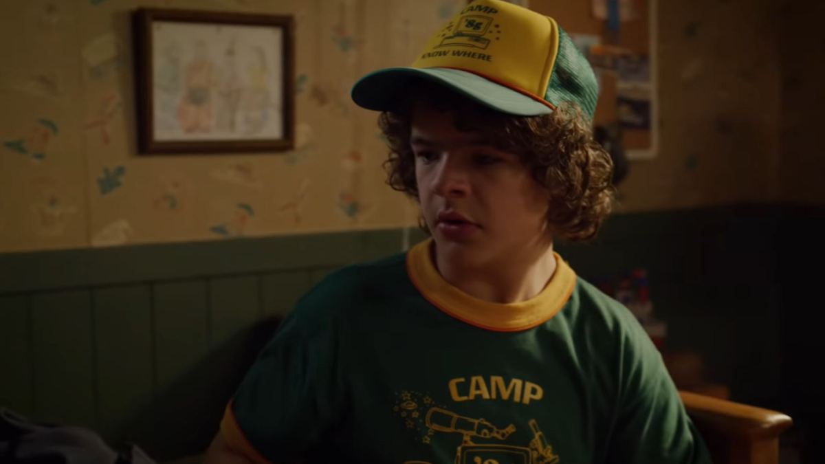 Dustin porte une casquette et un t Shirt « Camp Know Where » dans la saison 3. // Source : Youtube/Netflix Dustin porte une casquette et un t Shirt « Camp Know Where » dans la saison 3. // Source : Youtube/Netflix