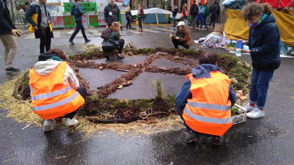 Les militants bâtissent des zones « naturelles », avec de la terre et des plantes récupérées dans des poubelles ou offertes par des habitants. Ici, c'est le logo de XR qui est représenté. // Source : Numerama Les militants bâtissent des zones « naturelles », avec de la terre et des plantes récupérées dans des poubelles ou offertes par des habitants. Ici, c'est le logo de XR qui est représenté. // Source : Numerama