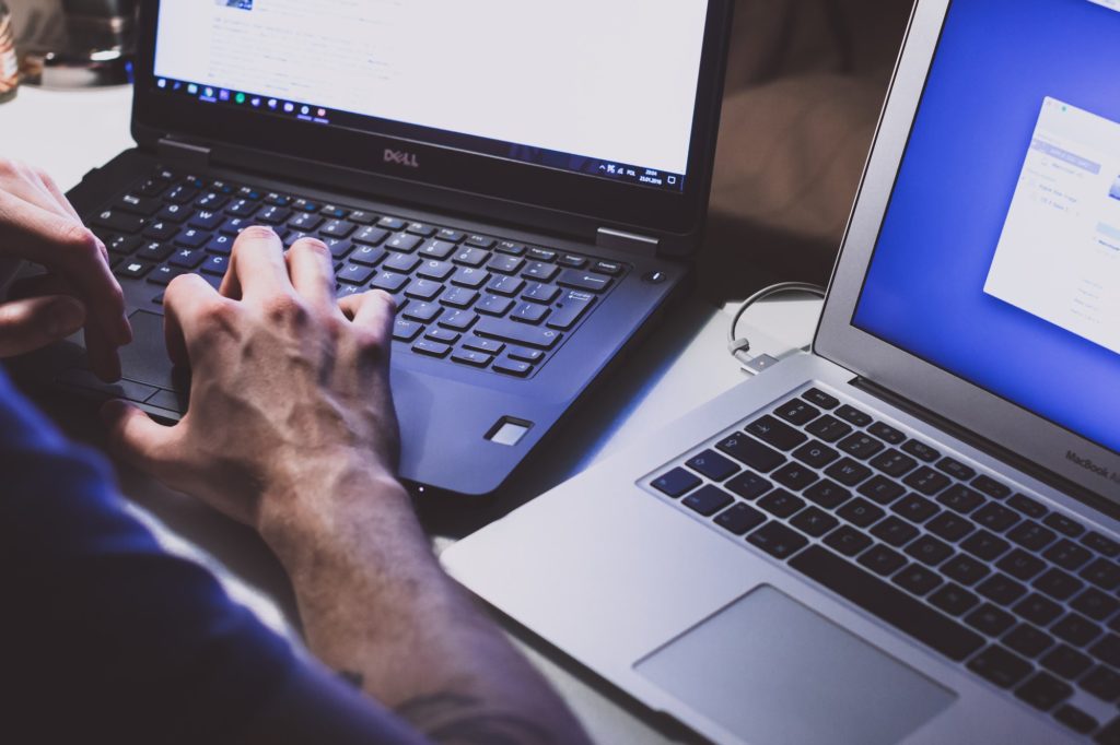 Un homme avec des mains de hacker et deux ordinateurs (probablement avec des malwares) // Source : Freestocks.org via Unsplash Un homme avec des mains de hacker et deux ordinateurs (probablement avec des malwares) // Source : Freestocks.org via Unsplash