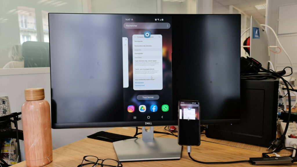 Le teléphone branché a l'écran duplique son affichage et permet la navigation au clavier et à la souris au sein de l'interface // Source : Photo Numerama Le teléphone branché a l'écran duplique son affichage et permet la navigation au clavier et à la souris au sein de l'interface // Source : Photo Numerama