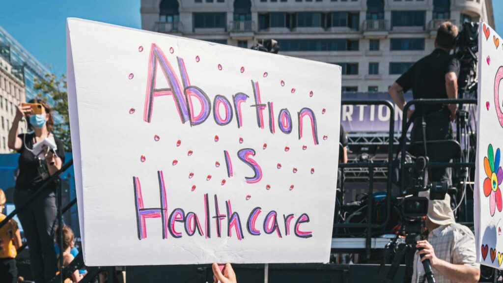 Une pancarte pendant une manifestation en soutien au droit à l'IVG, qui dit « l'avortement fait partie des soins de santé » // Source : Gayatri Malhotra / Unsplash Une pancarte pendant une manifestation en soutien au droit à l'IVG, qui dit « l'avortement fait partie des soins de santé » // Source : Gayatri Malhotra / Unsplash