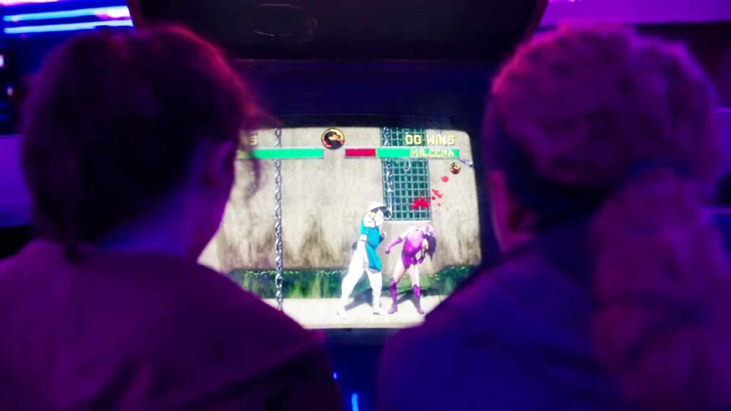 Ellie et Riley jouent à Mortal Kombat II sur une machine d'origine, mais avec un écran LED // Source : HBO Ellie et Riley jouent à Mortal Kombat II sur une machine d'origine, mais avec un écran LED // Source : HBO