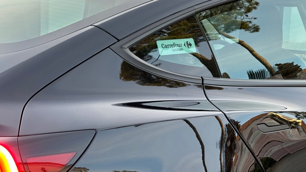 Sur la vitre arrière de la Model 3, il y a un autocollant Carrefour. // Source : Numerama Sur la vitre arrière de la Model 3, il y a un autocollant Carrefour. // Source : Numerama