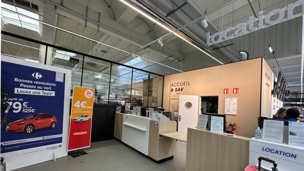 L'agence Carrefour Location est collée à l'accueil du magasin. Deux voitures sont mises en avant : la Dacia et la Tesla. // Source : Numerama L'agence Carrefour Location est collée à l'accueil du magasin. Deux voitures sont mises en avant : la Dacia et la Tesla. // Source : Numerama