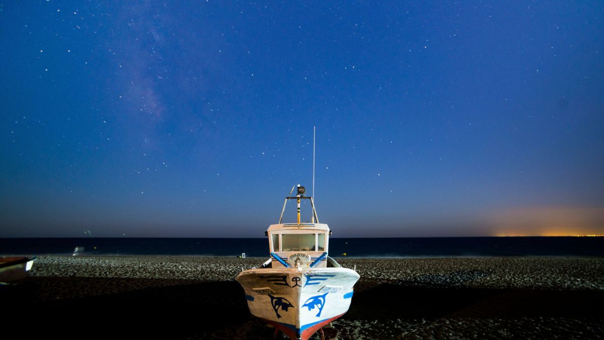 Bateau échoué sur une plage, sous un ciel étoilé. // Source : Canva Bateau échoué sur une plage, sous un ciel étoilé. // Source : Canva